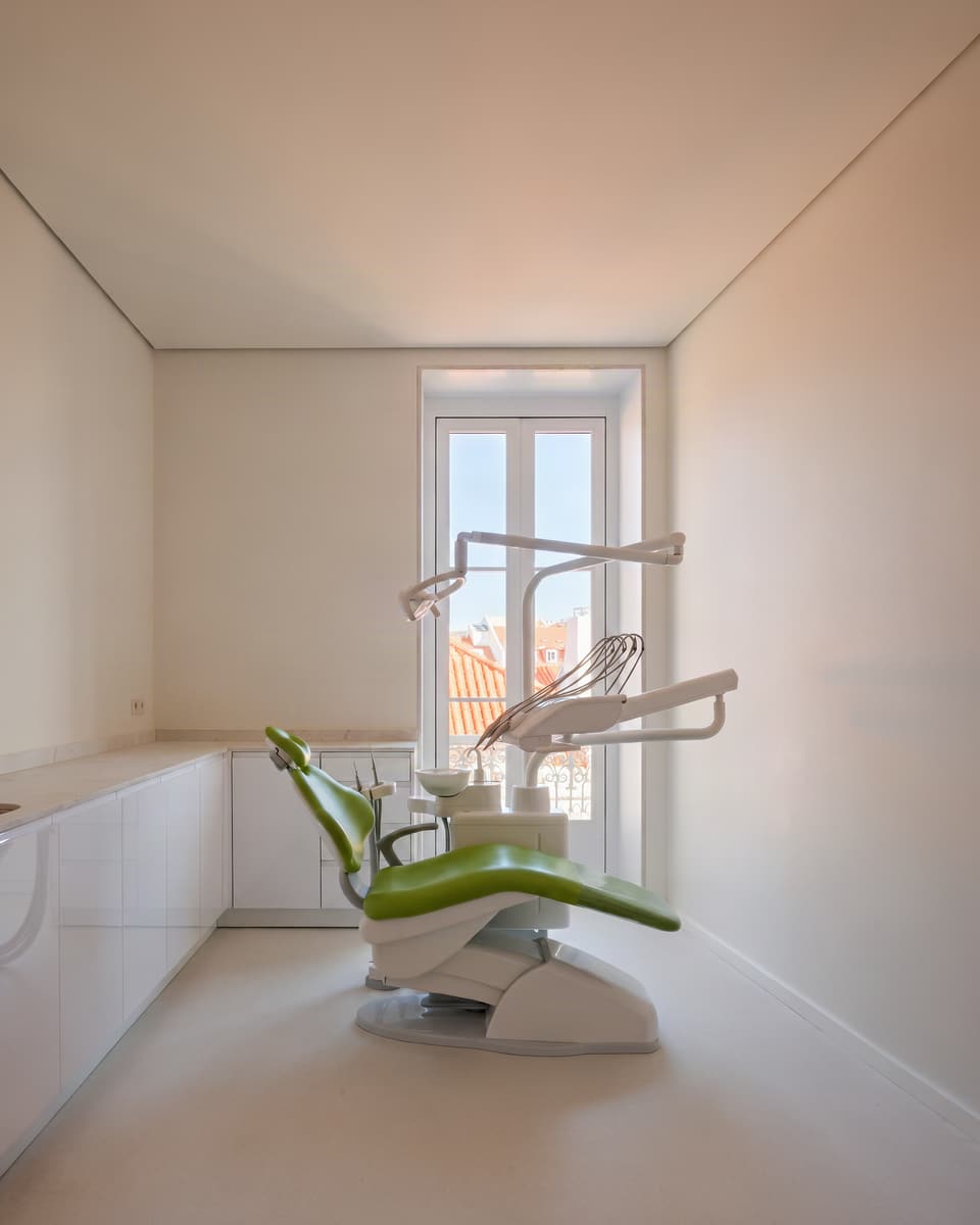 imagem ilustrativa: sala de tratamentos clara, com a cadeira verde e a cidade sugerida através do vidro